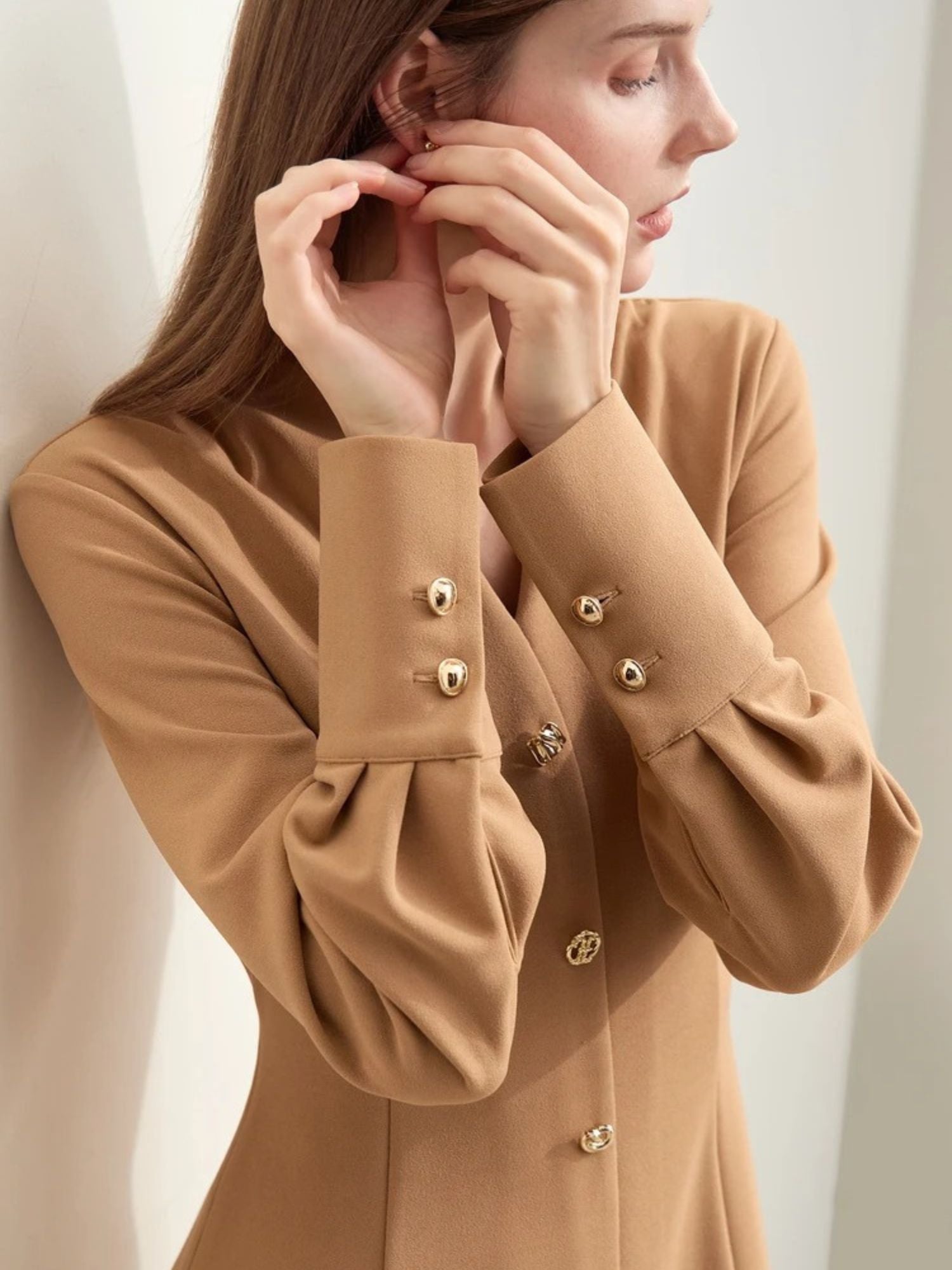 Beiges Midikleid mit V-Ausschnitt, Modell frontal mit Hand an der Wange.