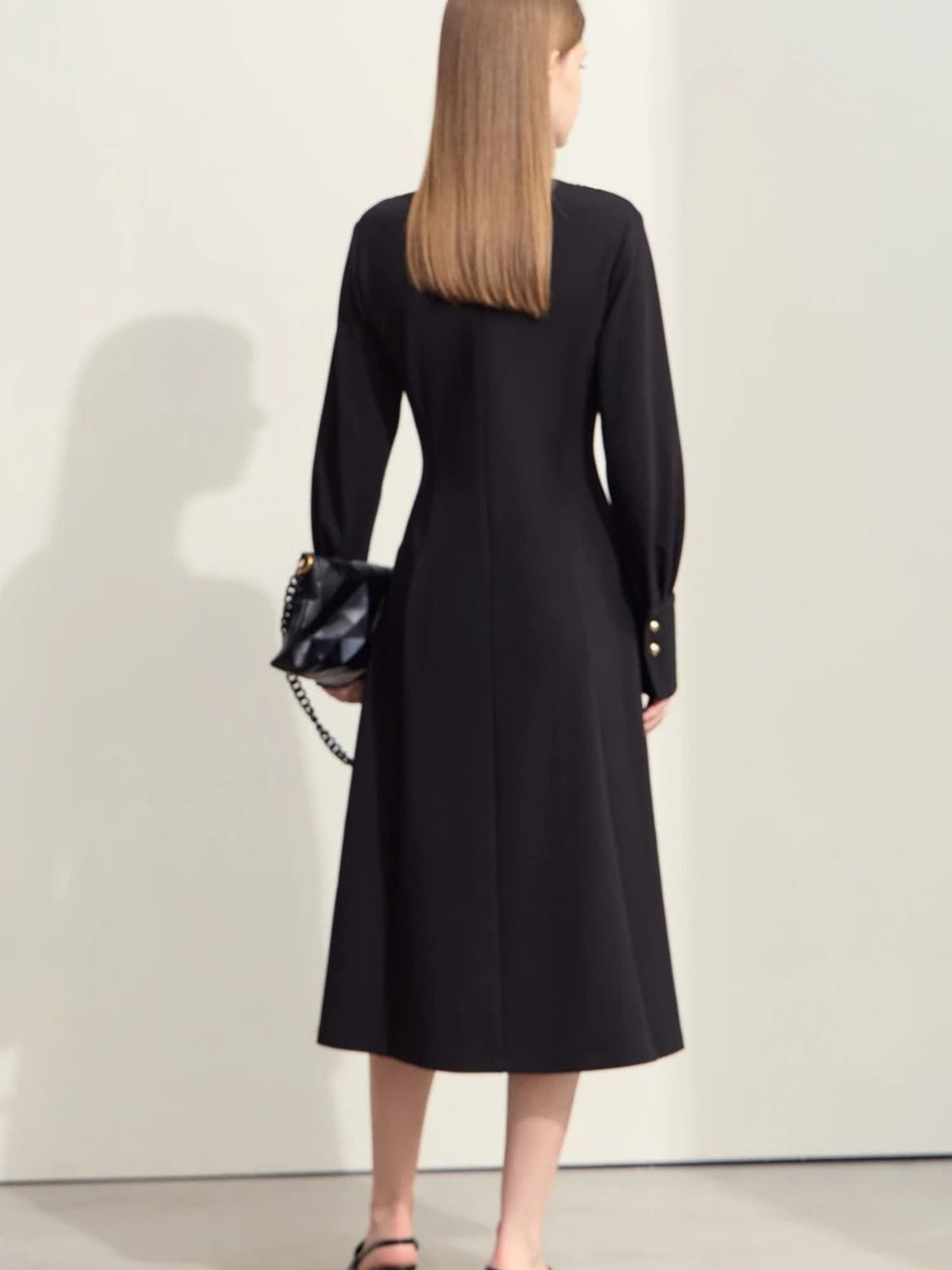 Schwarzes Midikleid, Rückansicht des Modells mit Handtasche.