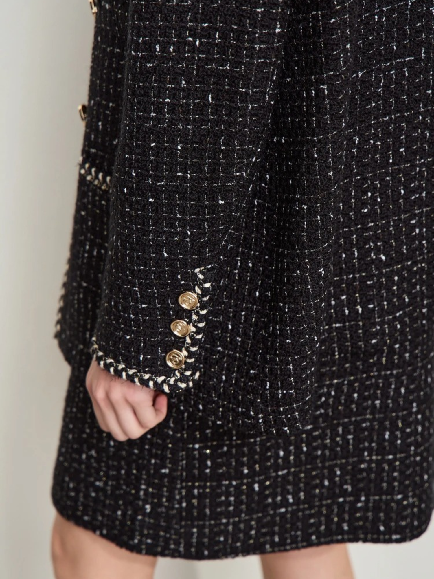 Detailaufnahme: Ärmelabschluss der schwarzen Tweed-Jacke mit Goldknöpfen.