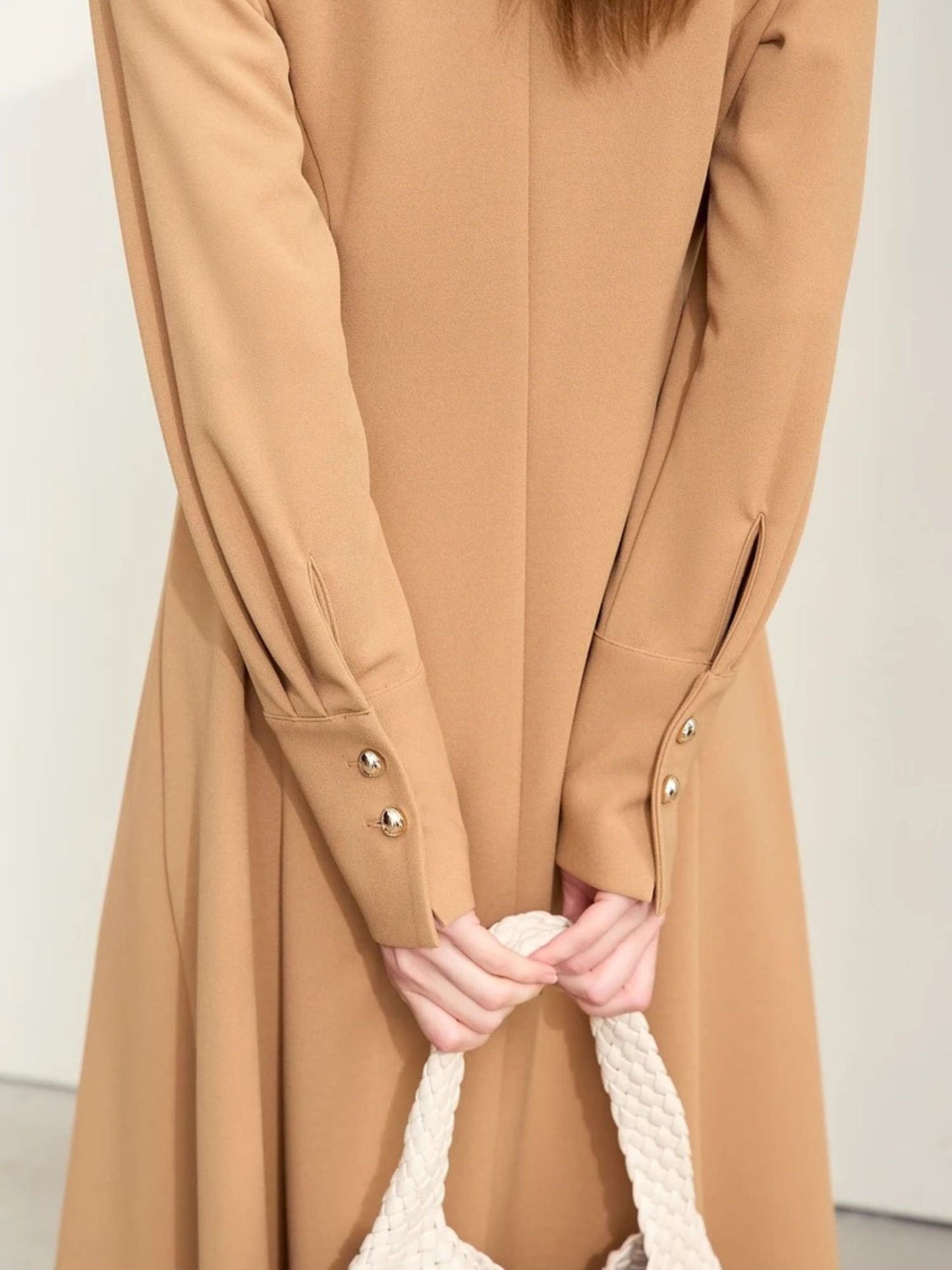 Detailaufnahme: Ärmeldetail mit Goldknöpfen am beigefarbenen Kleid.