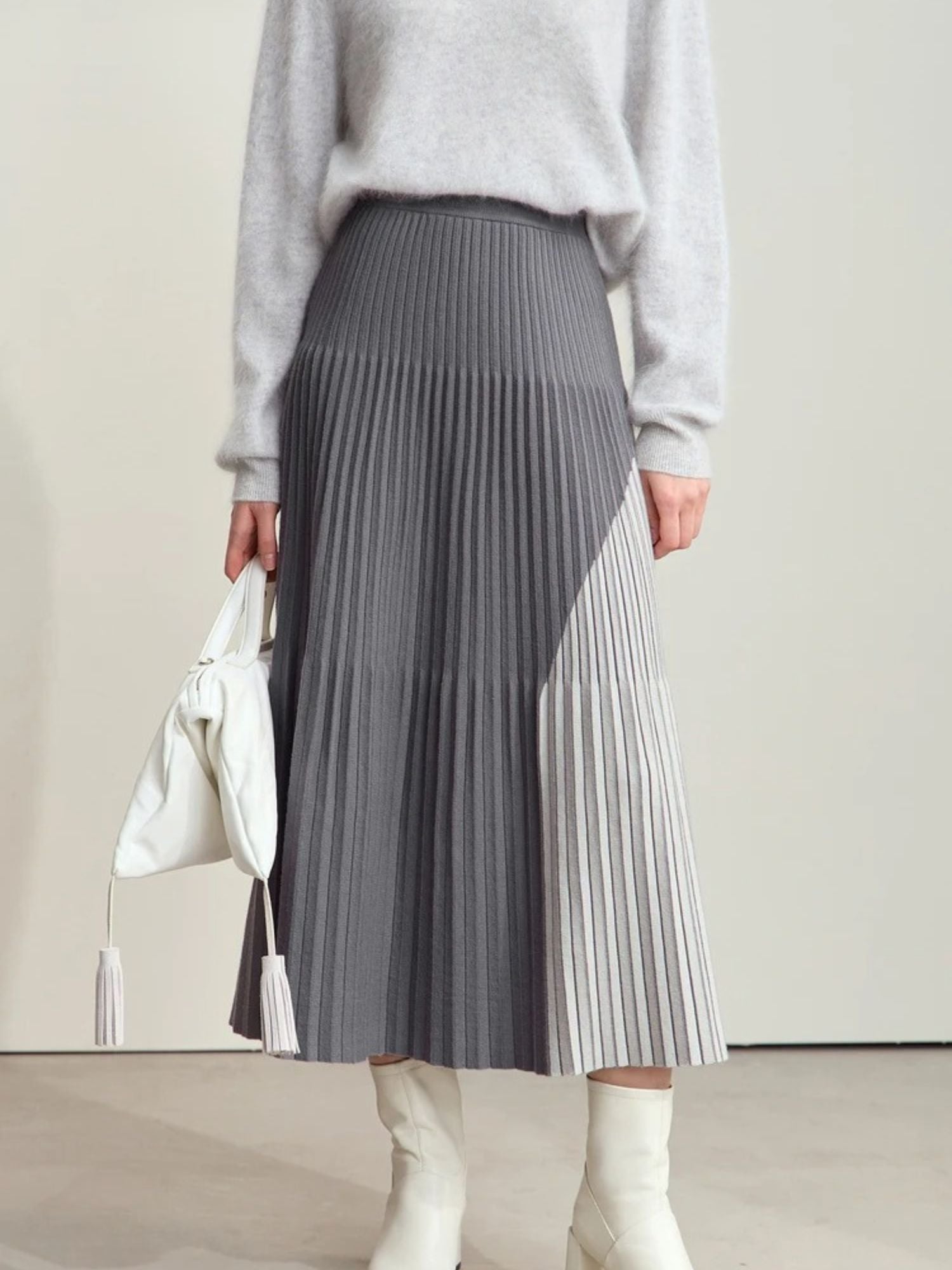 Grauer Plisseerock mit Farbkontrast, Modell frontal mit weißer Tasche.