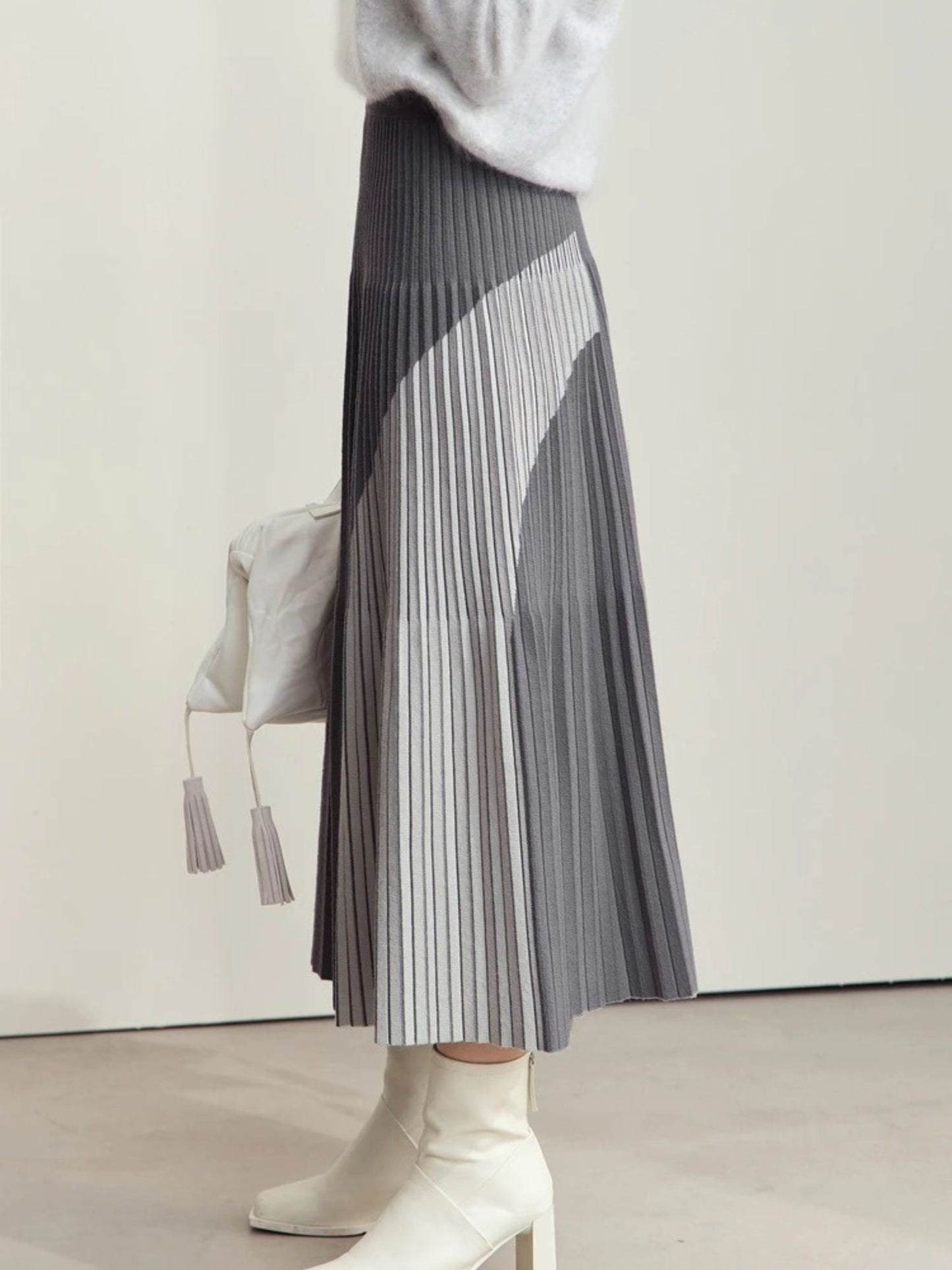Grau melierter Plisseerock mit asymmetrischem Design, Modell seitlich mit weißer Tasche.