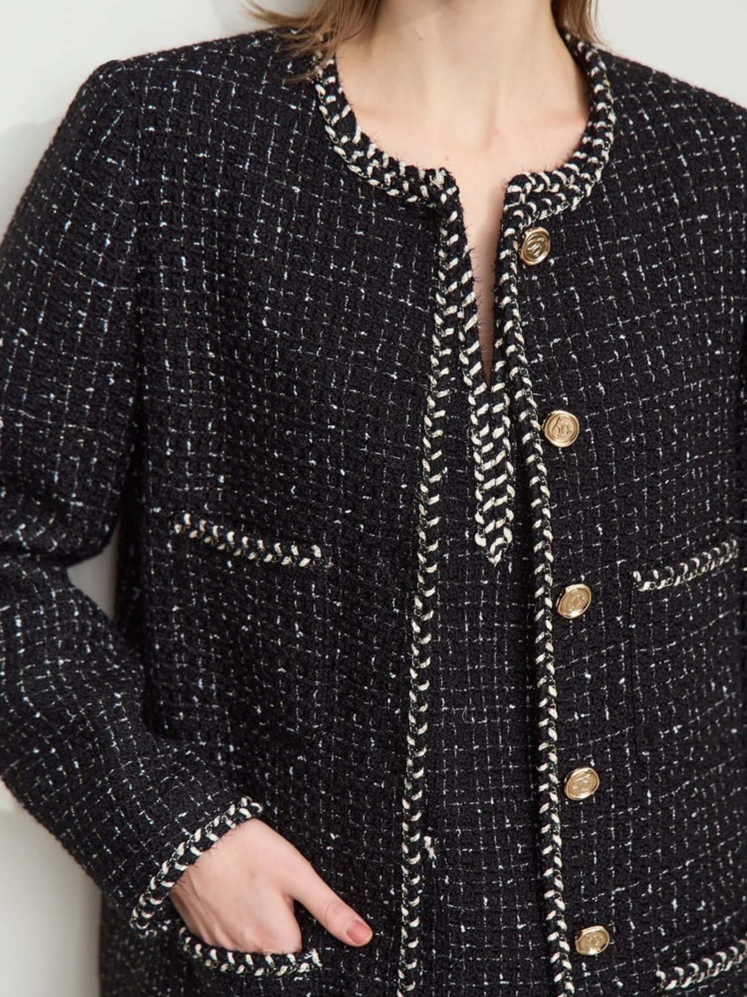 Detailaufnahme: Schwarze Tweed-Jacke mit Goldknöpfen und Rundhalsausschnitt.

