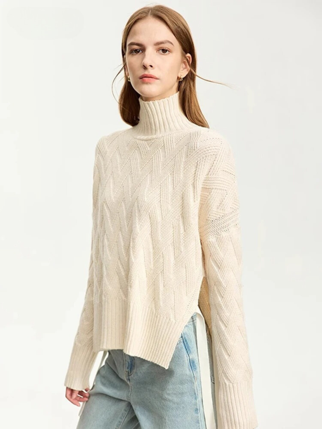 A woman wearing a turtle neck knit sweater with a tie design on the side in a cream color.