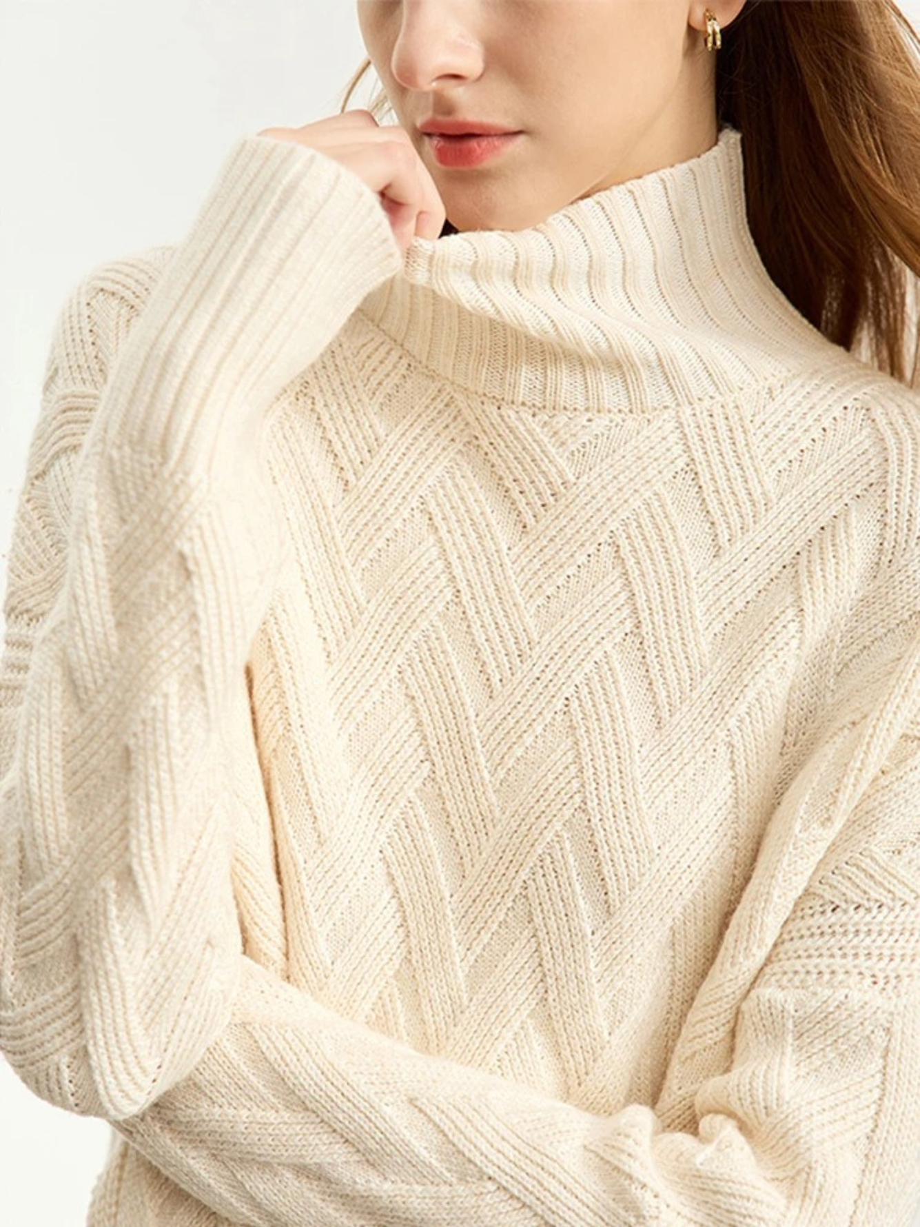 A woman wearing a turtle neck knit sweater with a tie design on the side in a cream color.