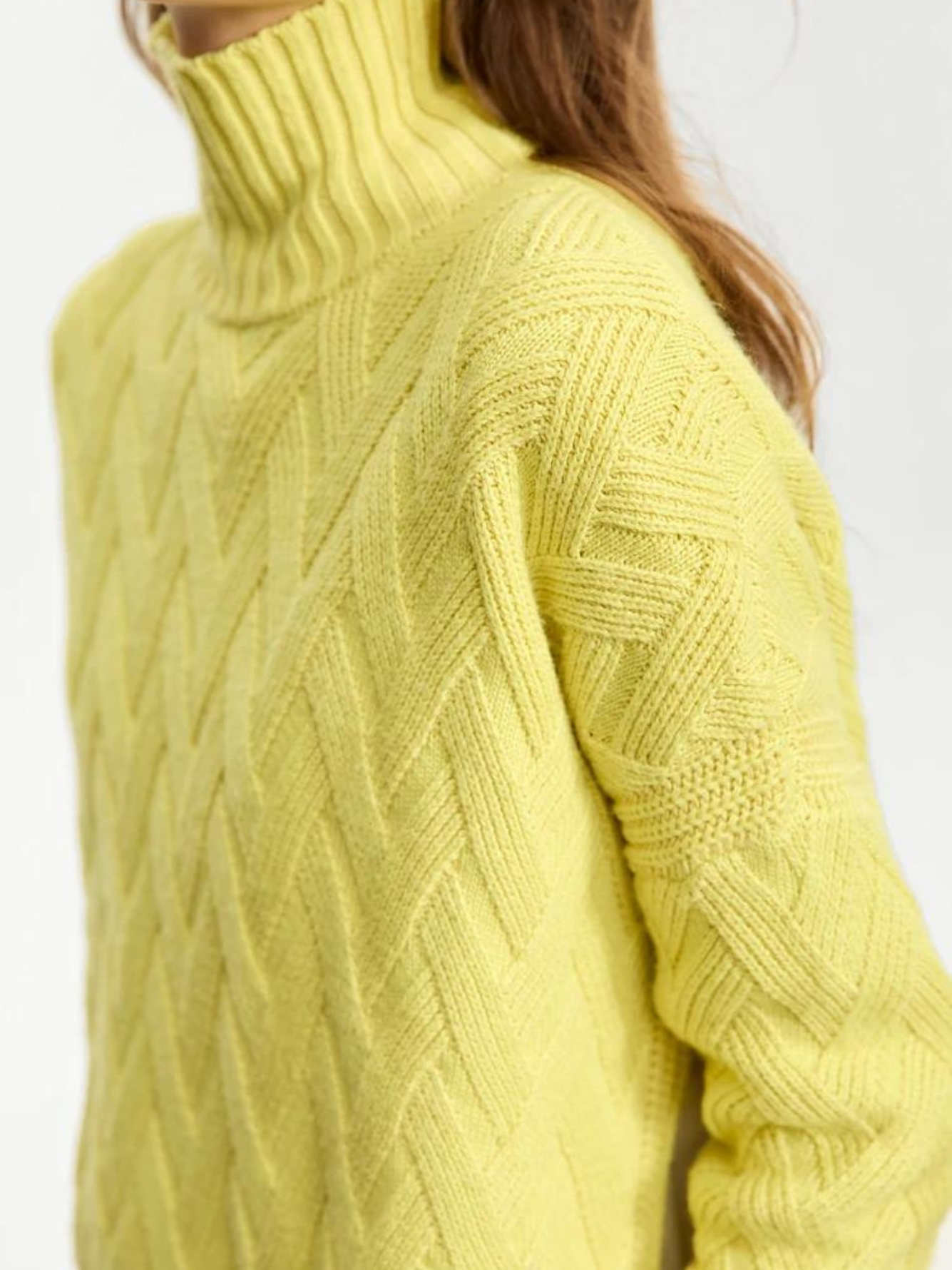 Close up of a woman wearing a turtle neck knit sweater with a tie design on the side in a lime green color