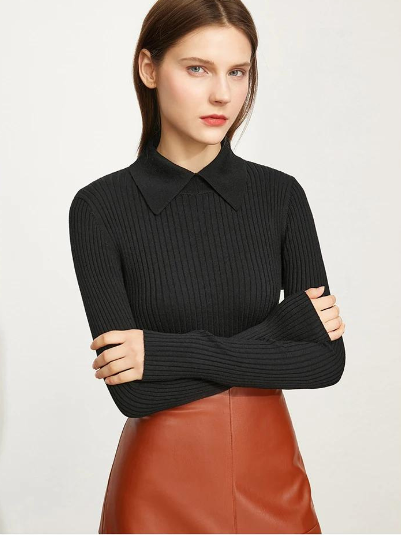 A woman wearing a ribbed sweater with a classic polo collar in black with a brown leather skirt.