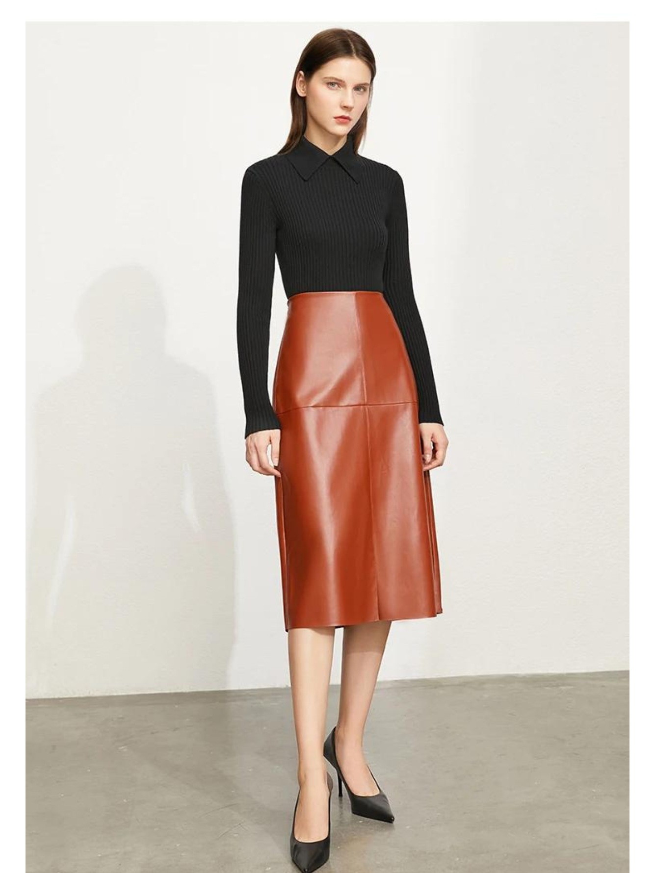A woman wearing a ribbed sweater with a classic polo collar in black with a brown leather skirt and black heels.
