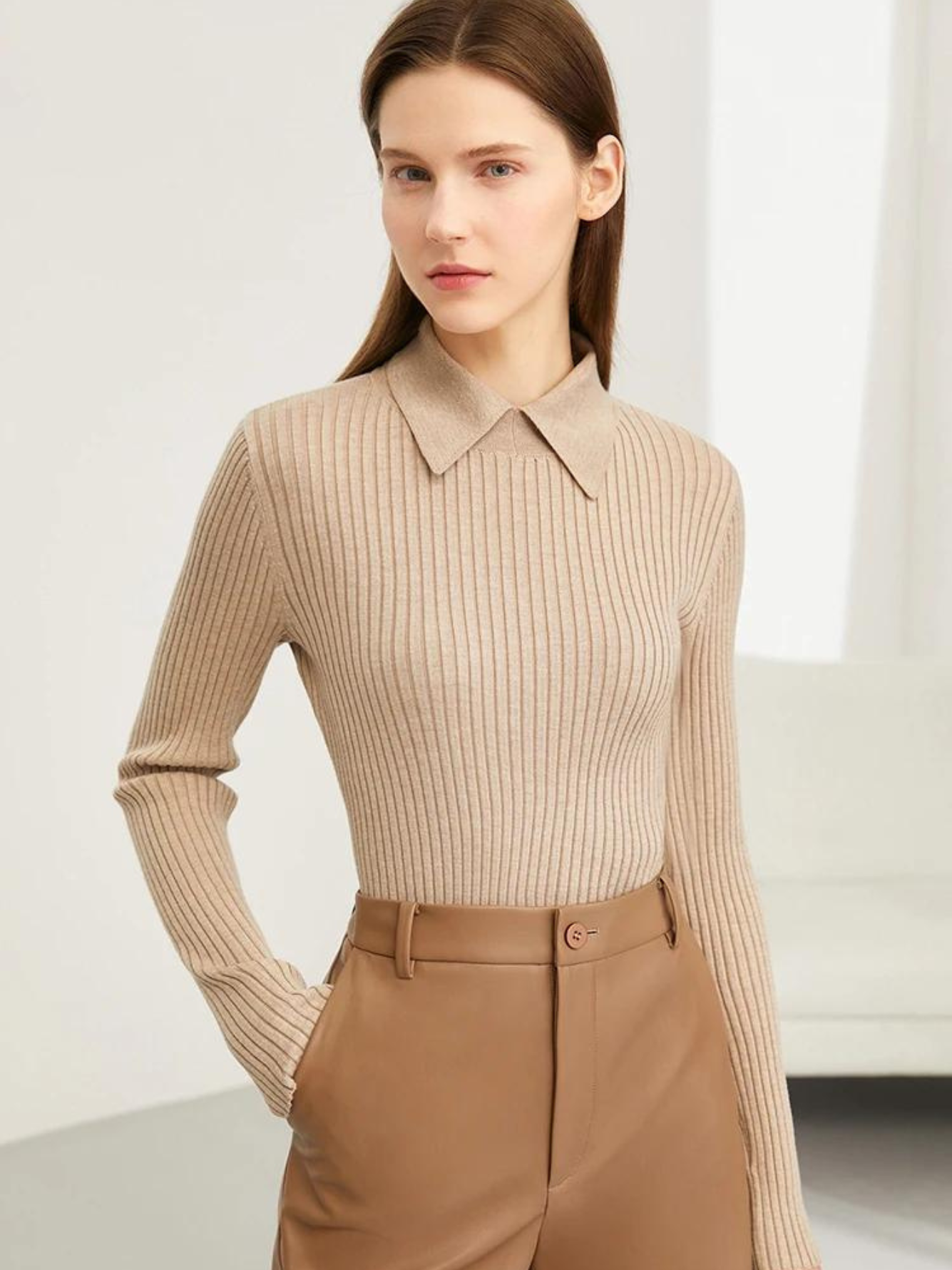 A woman wearing a ribbed sweater with a classic polo collar in khaki with a pair of brown leather shorts.