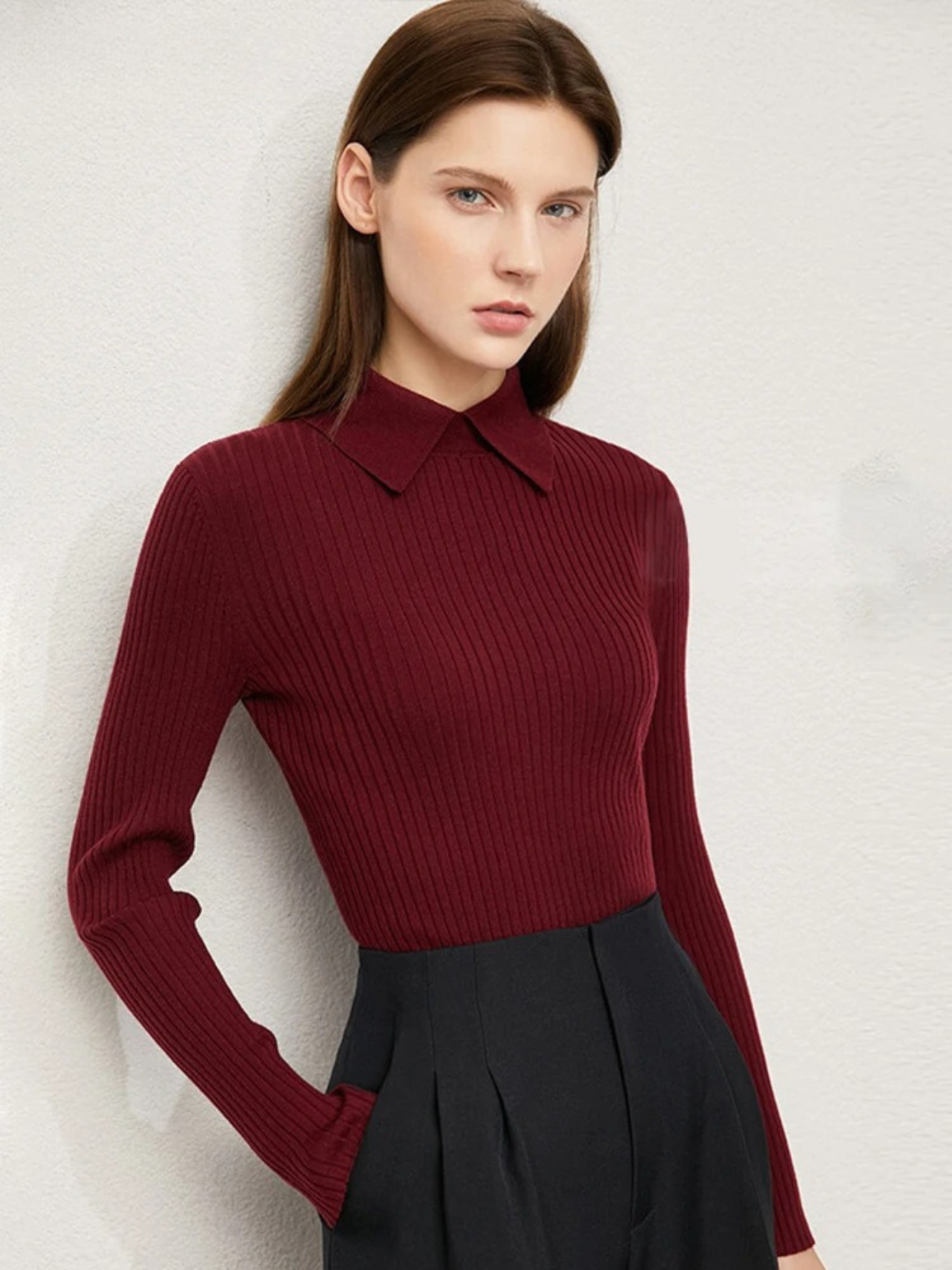 A woman wearing a ribbed sweater with a classic polo collar in a wine red color with a pair of black high waisted trousers.