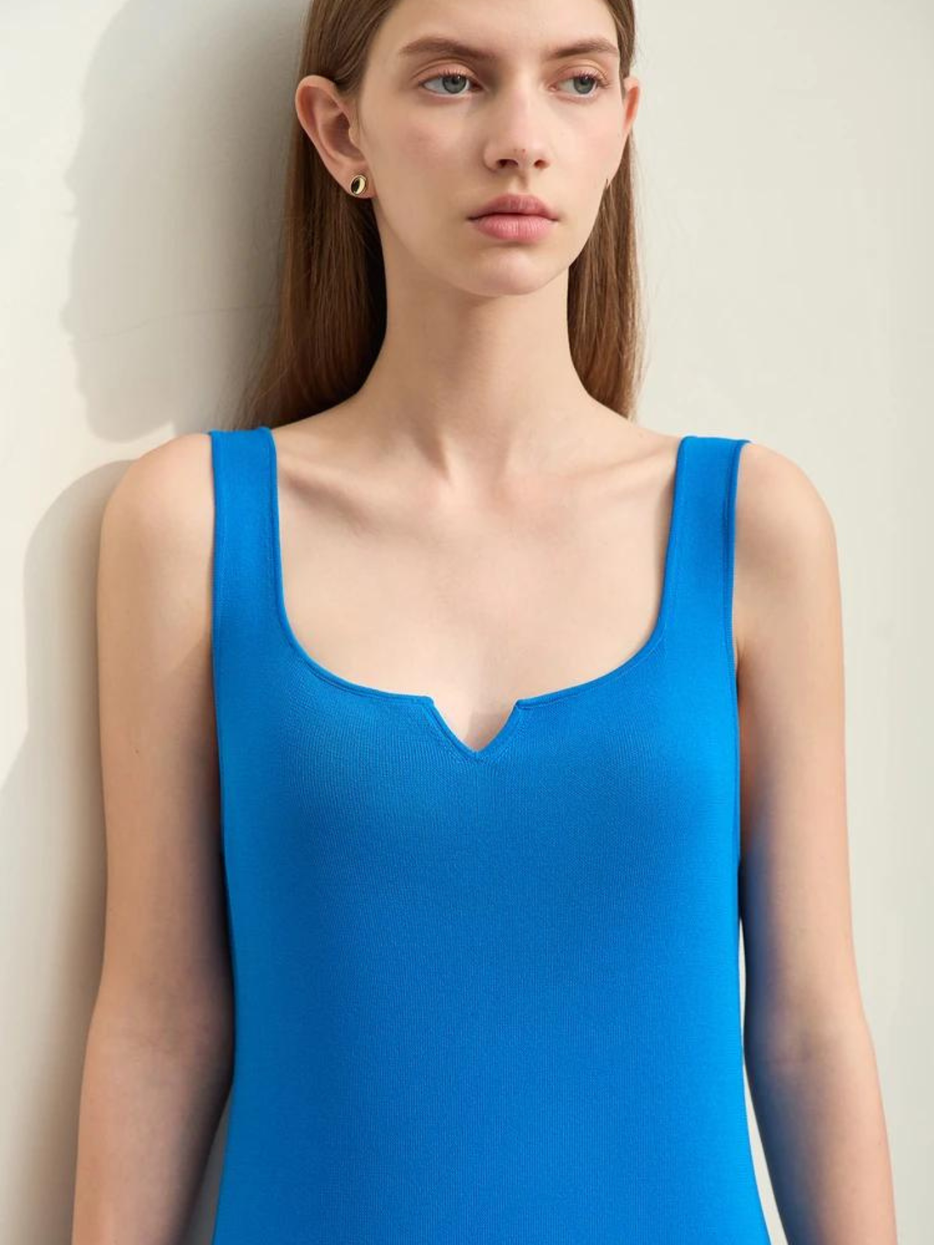 A woman wearing a plain, minimalist, sleeveless midi dresses with a v-cut out in the neckline in blue.