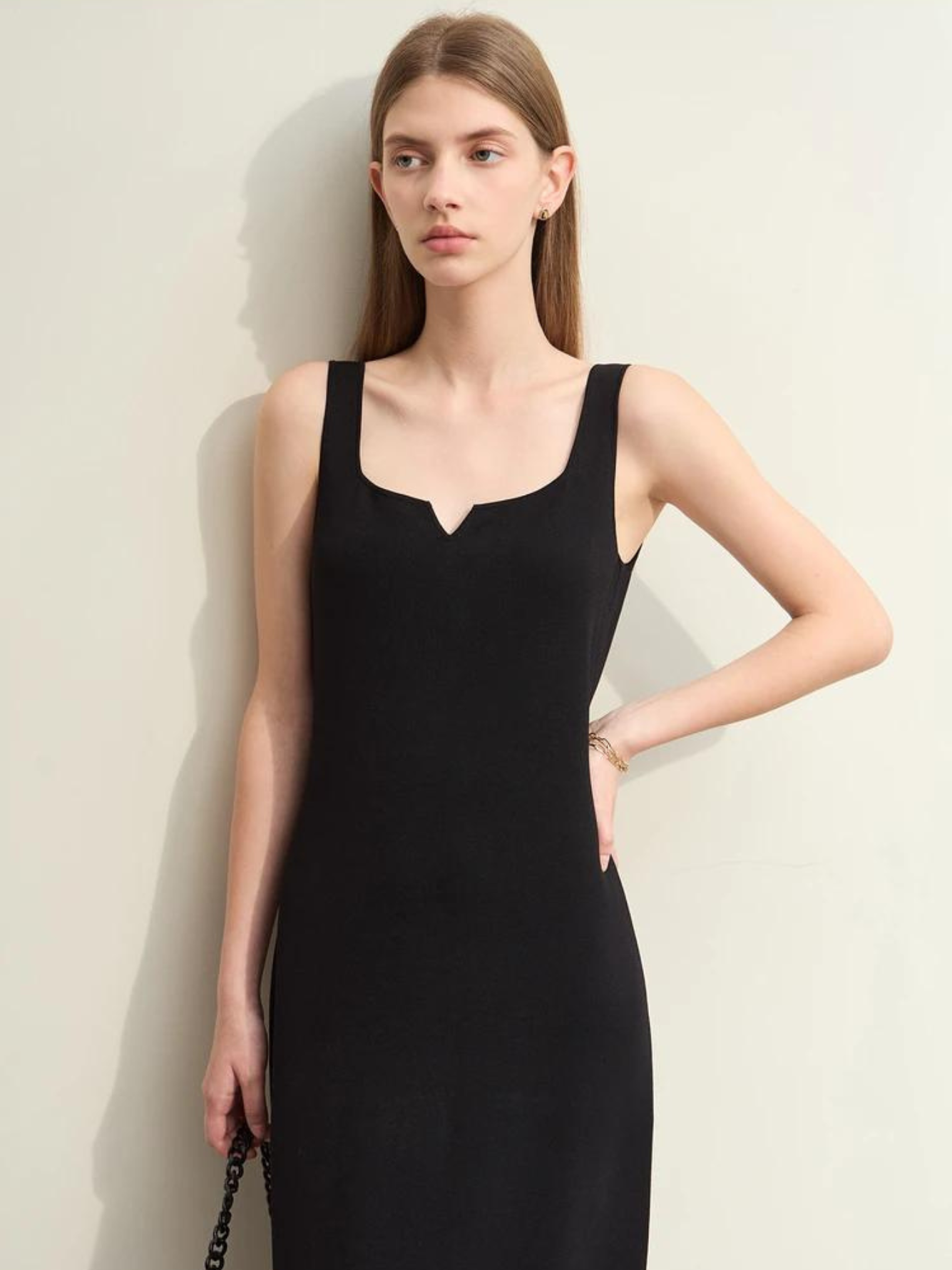 A woman wearing a simple, minimalist, sleeveless midi dresses with a v-cut out in the neckline in black. 