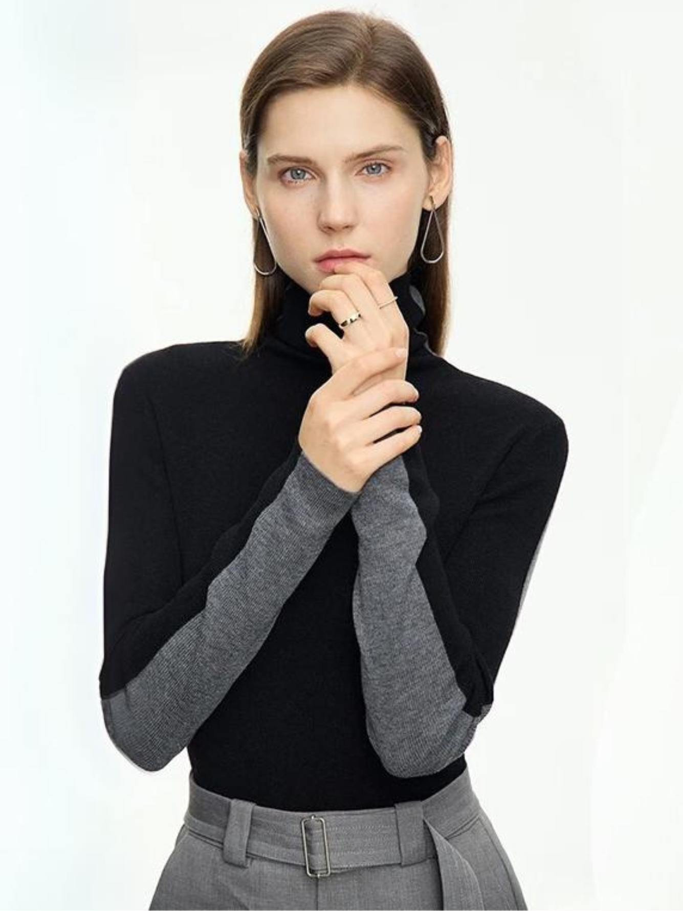 A woman wearing a mock neck, dual toned sweater in gray and black with a pair of gray belted high waisted pants with a belt detail.