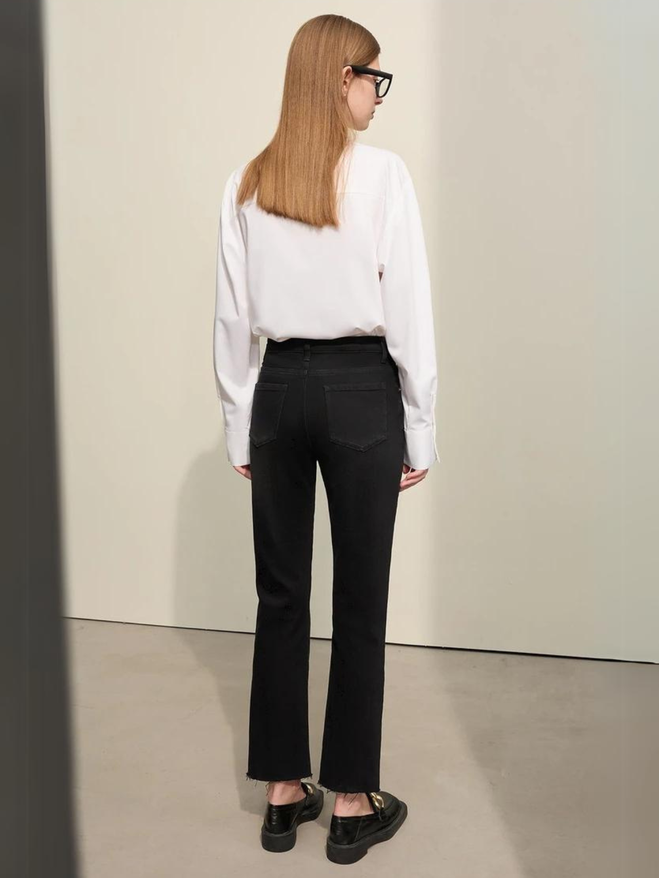 A woman wearing a classic white long sleeve shirt with a pair of black, pencil cut jeans and a pair of loafers.