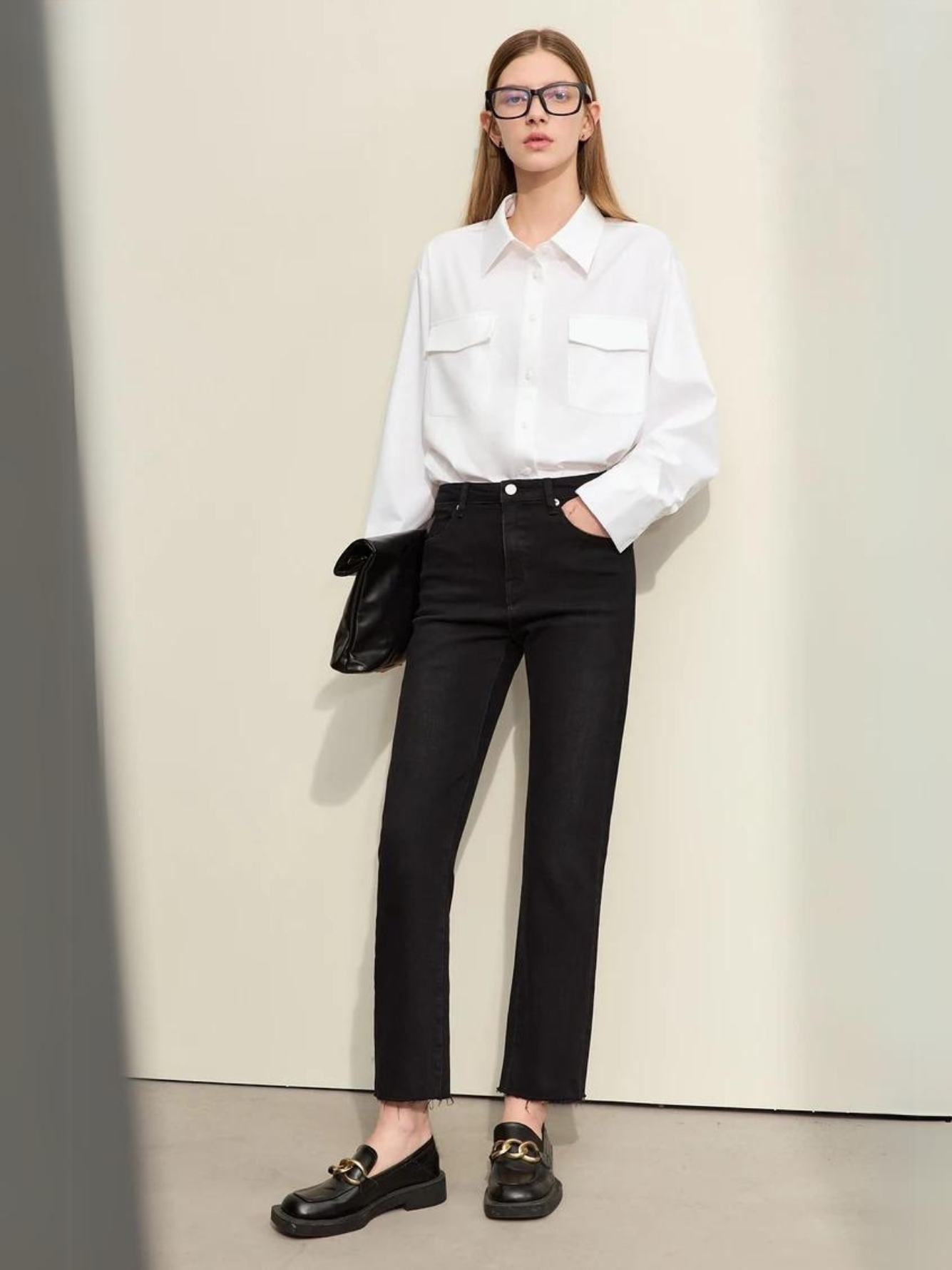 A woman wearing a classic white long sleeve shirt with a pair of black, pencil cut jeans and a pair of loafers.