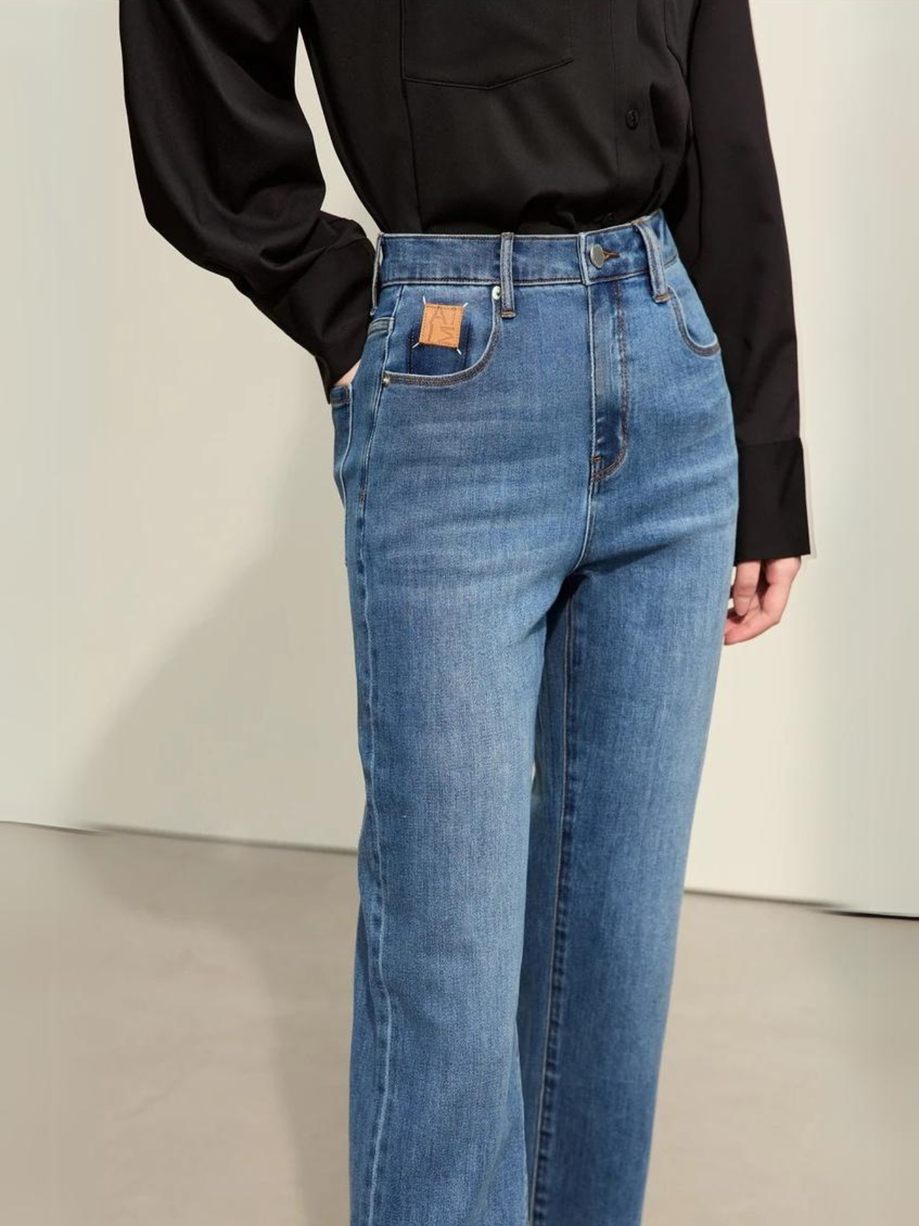 A woman wearing a classic black long sleeve shirt with a pair of denim blue, pencil cut jeans and a pair of loafers.