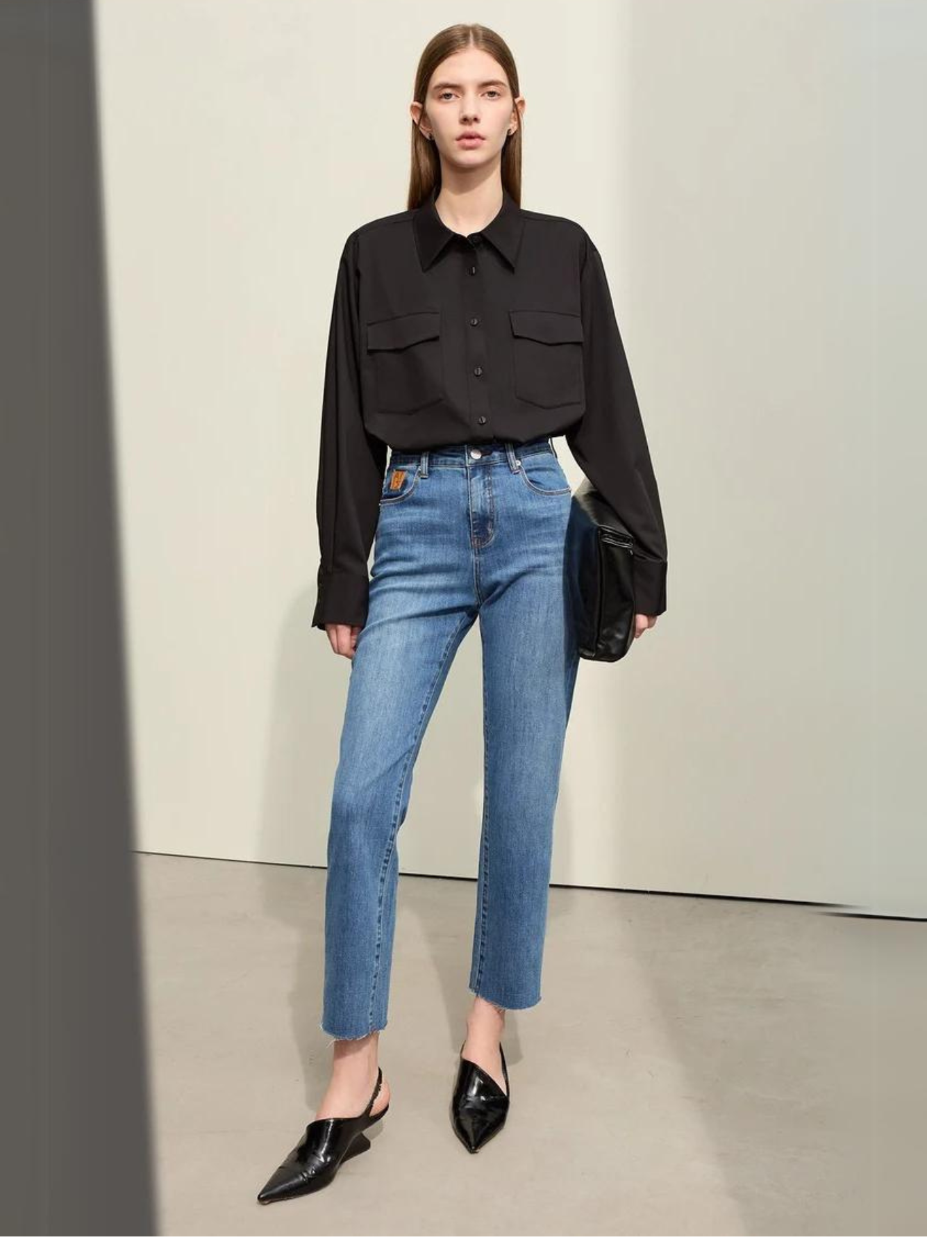 A woman wearing a classic black long sleeve shirt with a pair of denim blue, pencil cut jeans and a pair of pointed heels.